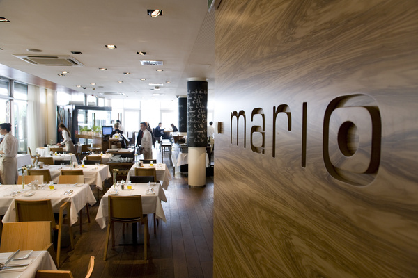 Modernes Restaurantinterieur mit hölzernen Akzenten, weißen Tischtüchern und einem Mario-Schild an der Wand.